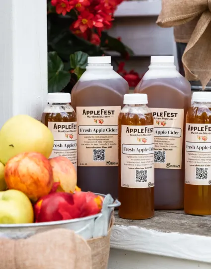 Bottles of apple cider beside a basket of apples.
