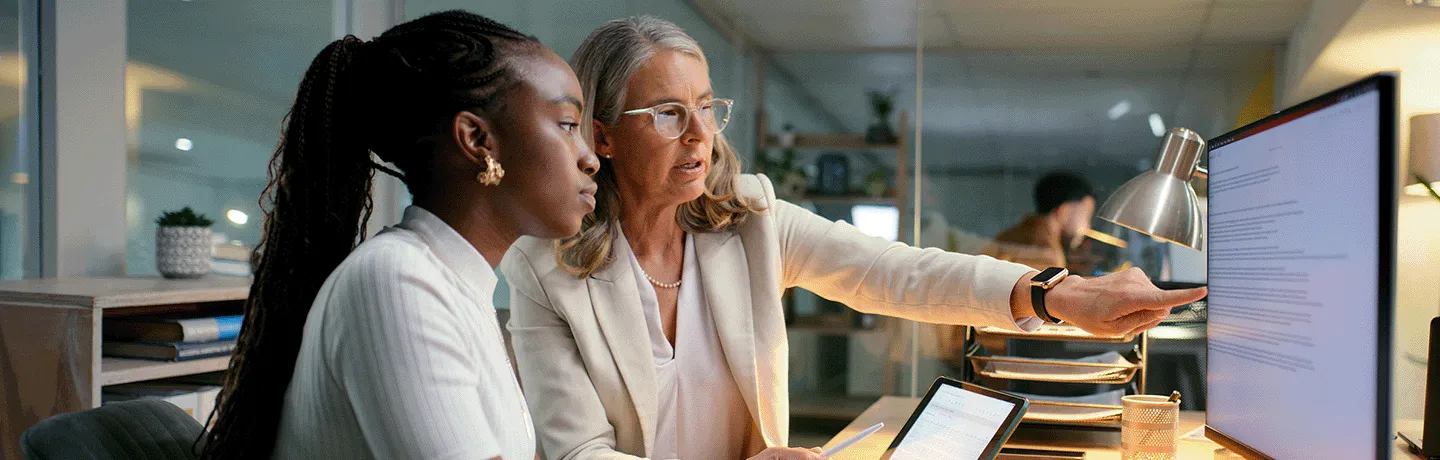 Older office employee demonstrating a task to a younger employee.