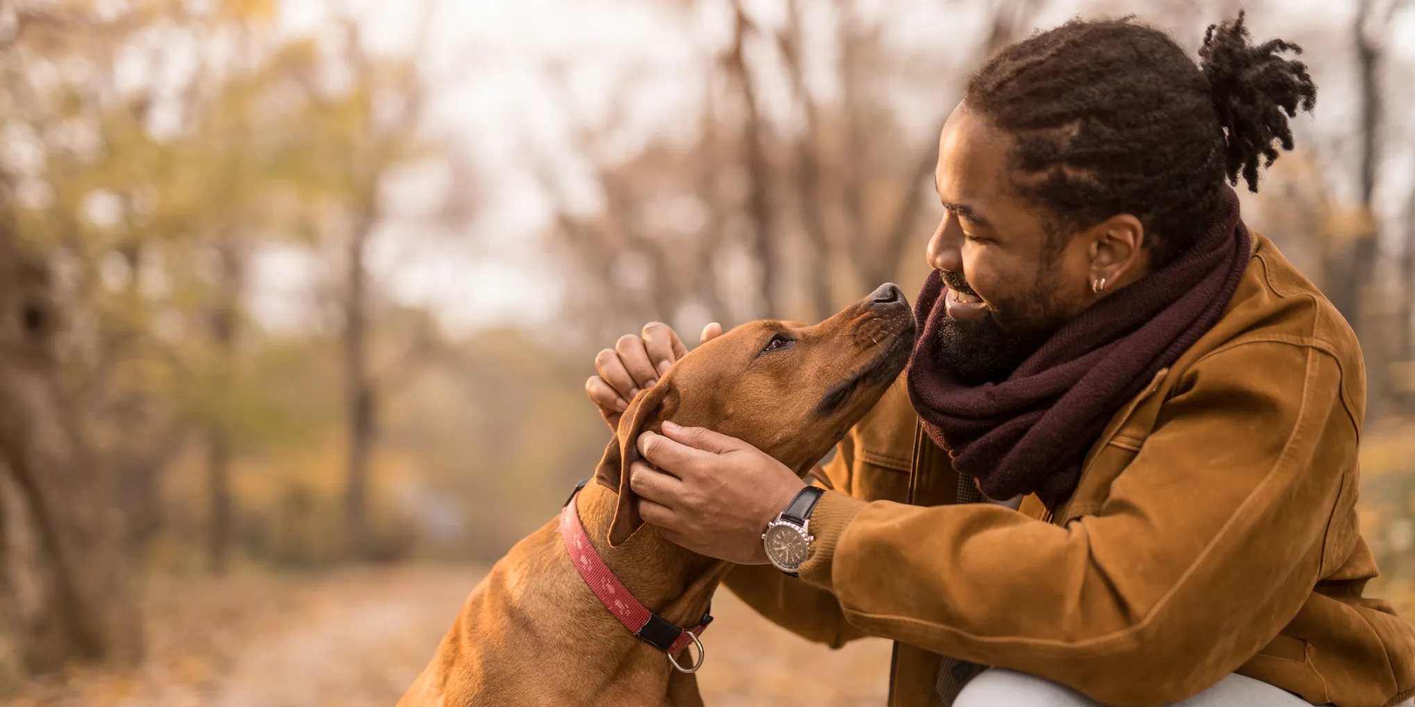 Person in outdoors smiling while petting a dog.